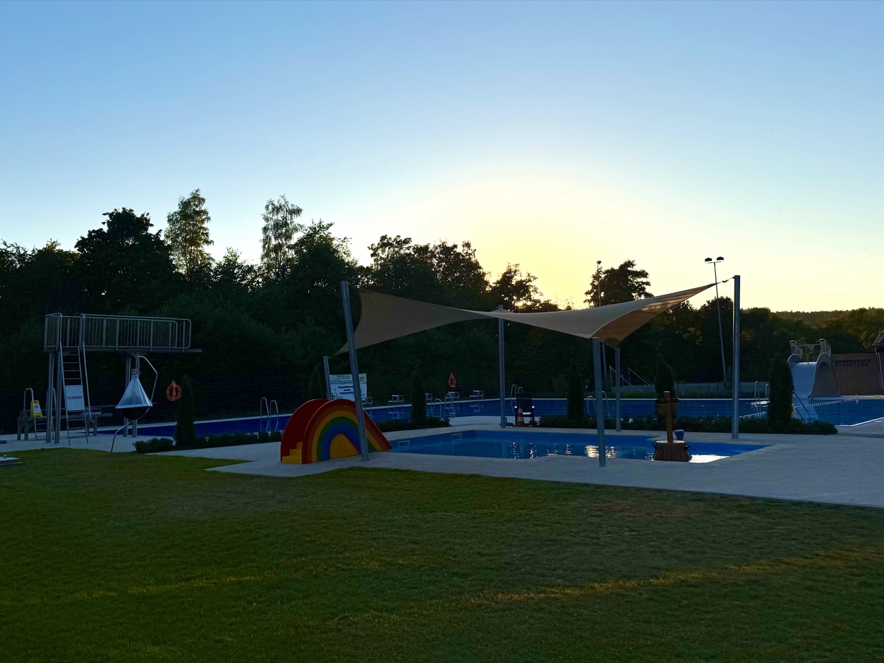 Freibad Rengshausen in der Abendsonne mit Sprungturm, Sonnensegel und Liegewiese
