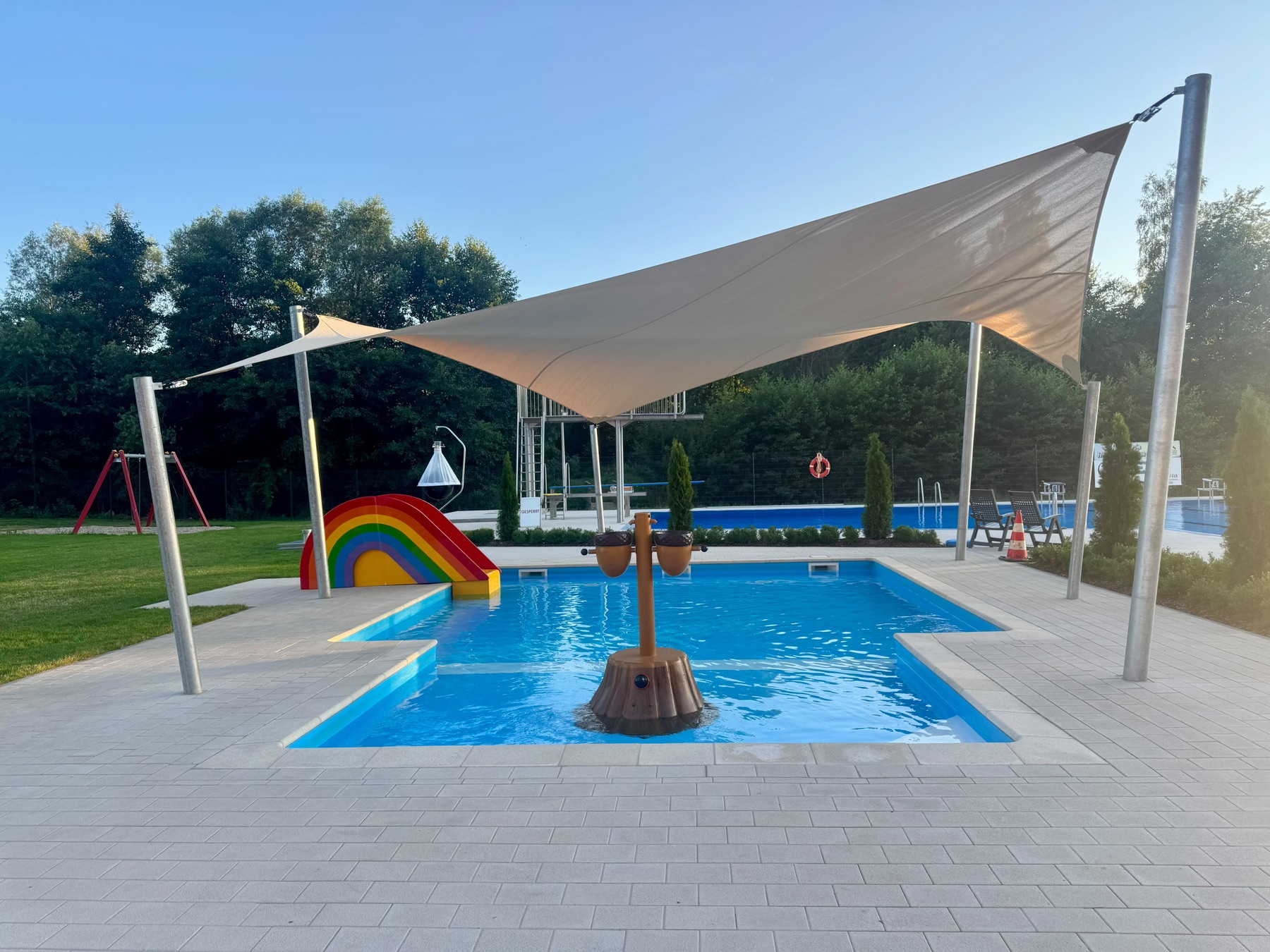 Kinderbecken mit Regenbogen-Rutsche und Wasserspiel unter dem Sonnensegel
