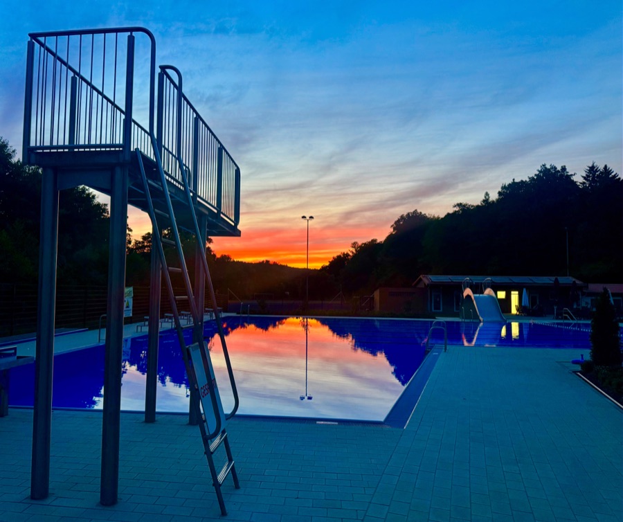 Sprungturm im Freibad Rengshausen bei Sonnenuntergang, das Becken spiegelt den Himmel