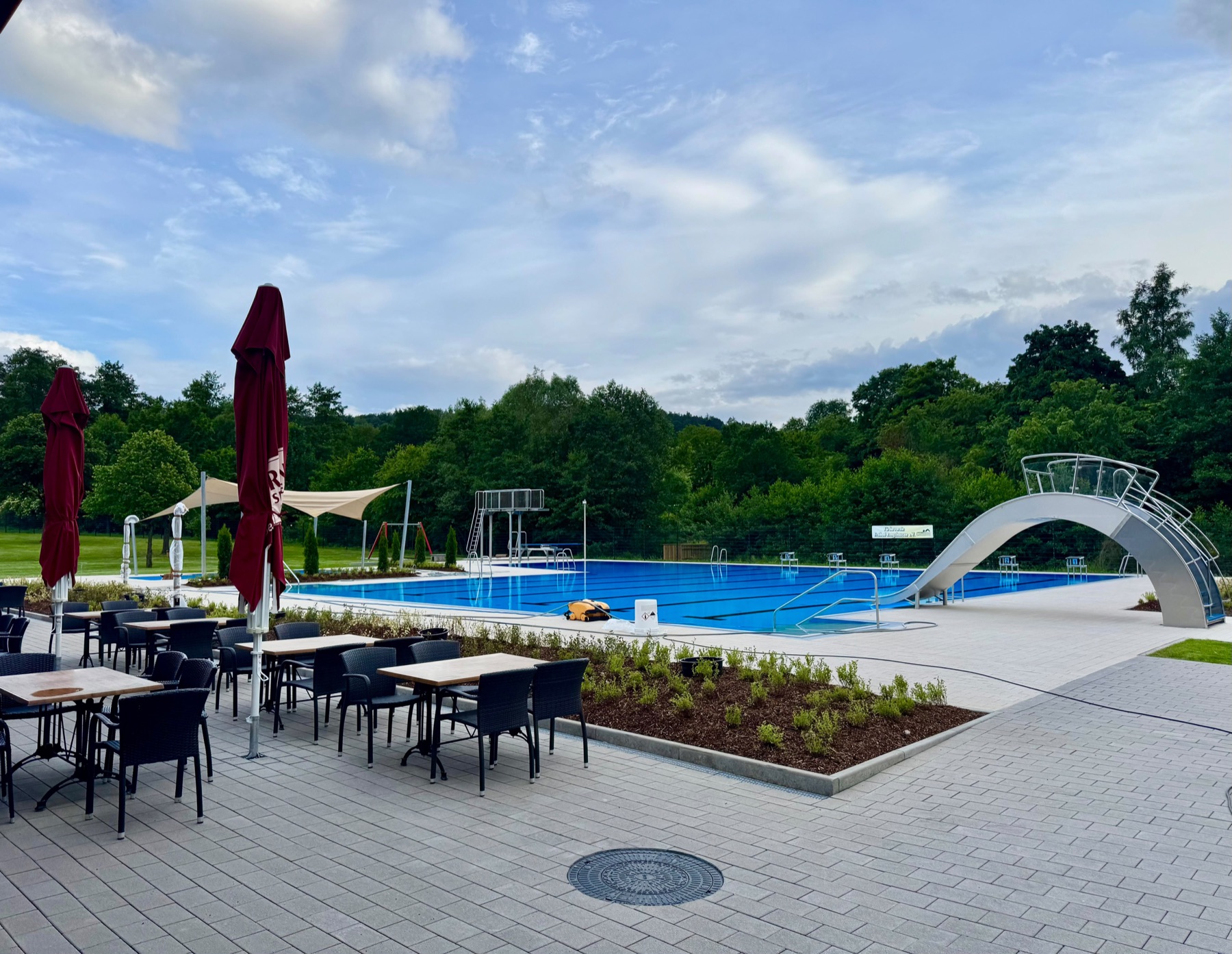Terrasse mit Tischen und Sonnenschirmen am Becken des Freibads Rengshausen