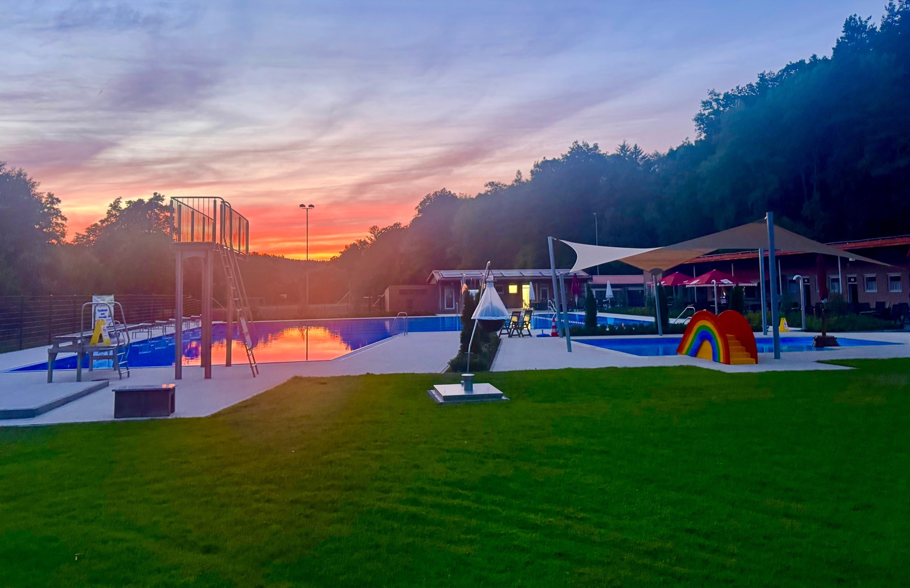 Liegewiese und Becken des Freibads Rengshausen in der Abenddämmerung